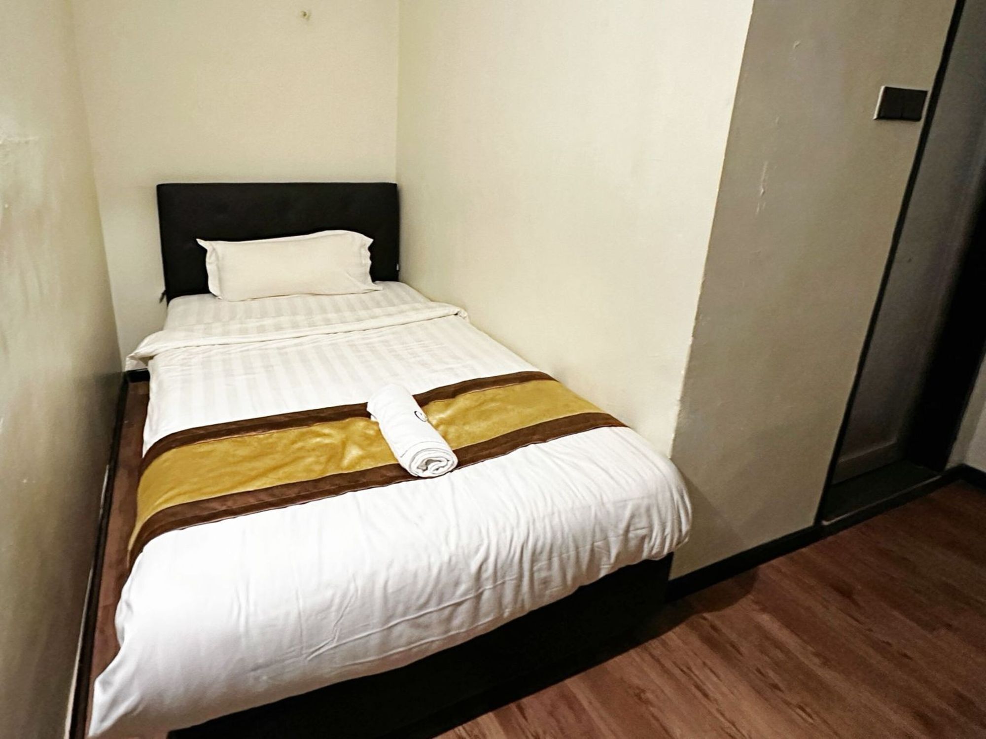 Uma cama de solteiro com colcha listrada em branco e castanho, uma toalha branca enrolada e uma cabeceira preta.