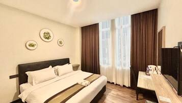 Habitación de hotel con cama, escritorio y televisor. Hay cortinas en las ventanas y una lámpara en el techo.