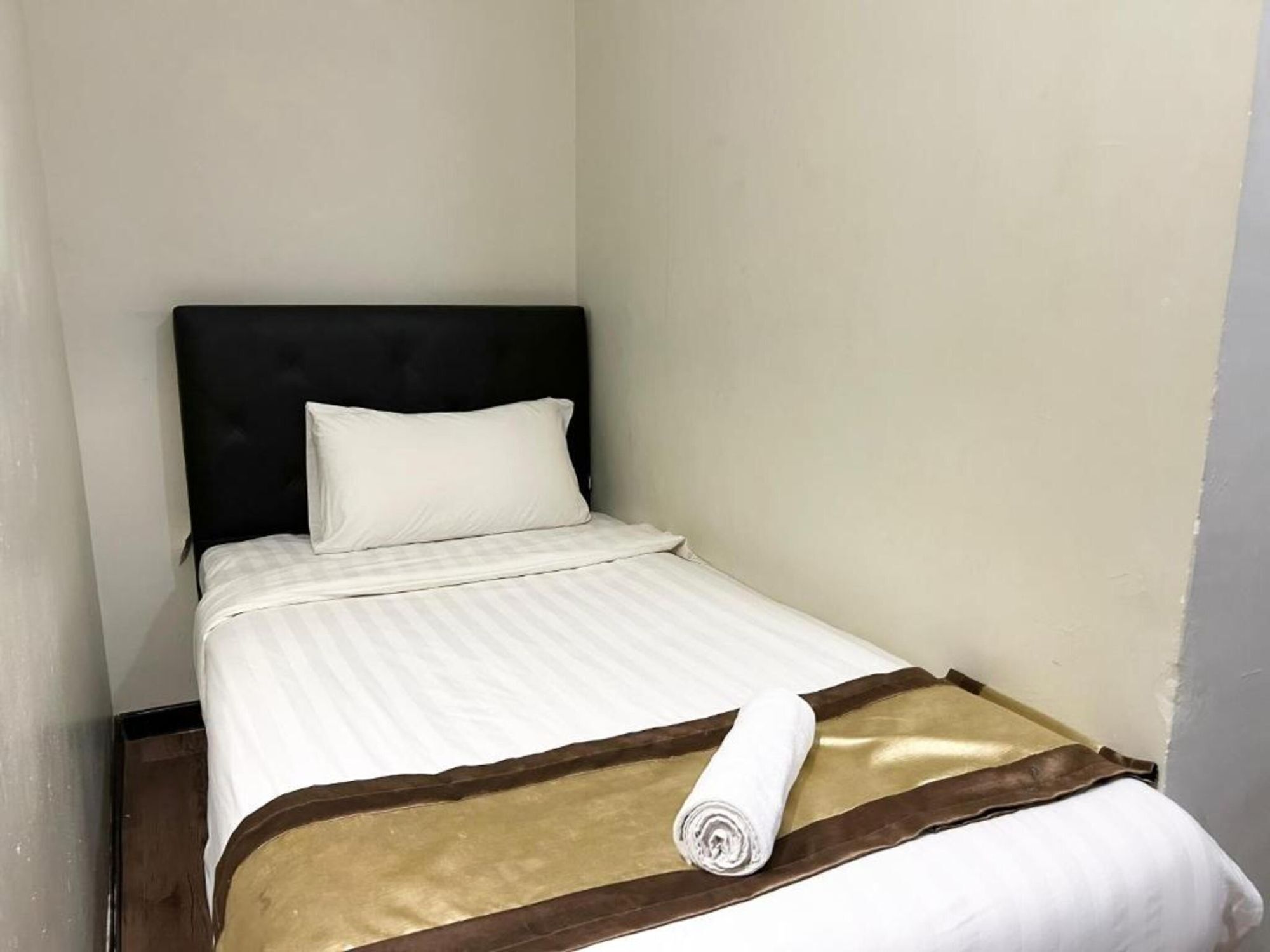 A small, neatly made bed with a white and brown striped bedspread, a rolled white towel, and a dark headboard.
