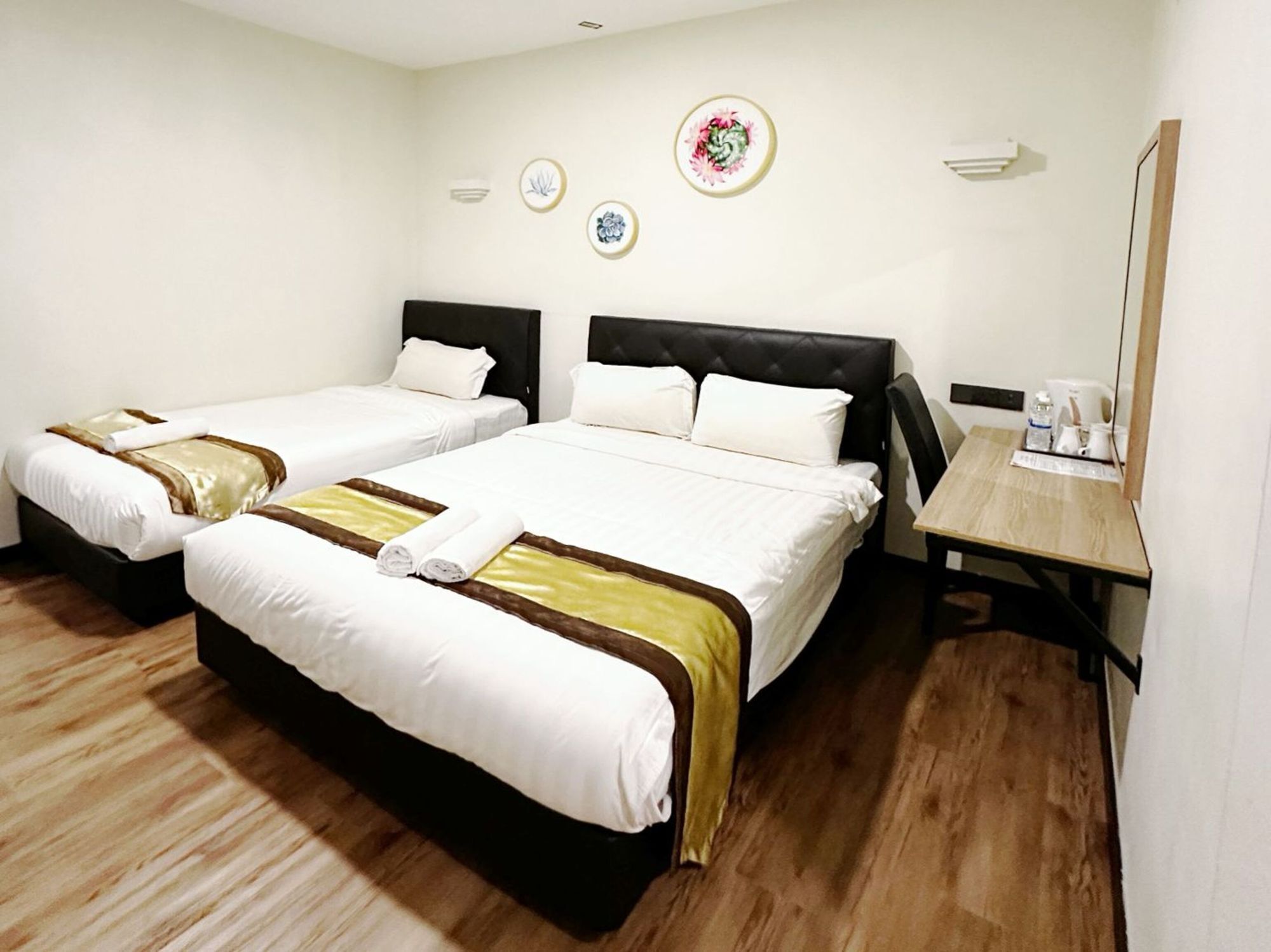 A hotel room with two beds, a wooden floor, a small table with a chair, and a wall-mounted air conditioning unit.