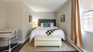 Un dormitorio con cama, mesita de noche, lámpara y ventana con cortinas.