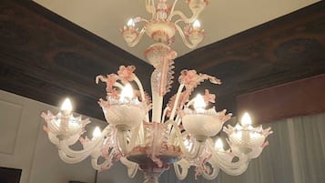 Un lampadario con bracci multipli e luci simili a candele, un quadro incorniciato al muro e una finestra con tende.