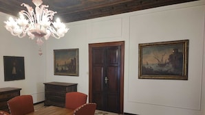 Un comedor con una mesa de madera, sillas rojas, una araña y tres cuadros en las paredes.