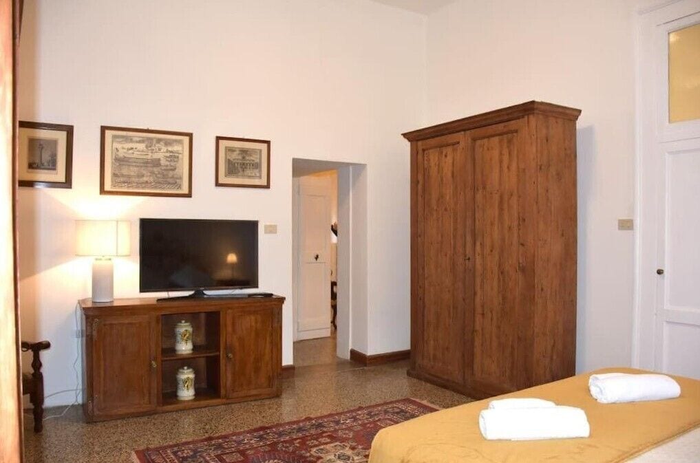 A hotel room with a bed, a television on a wooden cabinet, a wardrobe, and framed pictures on the wall.