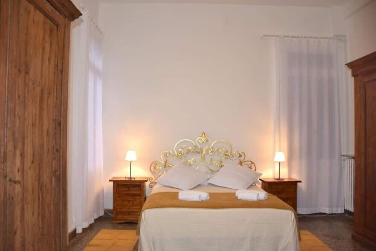 A bedroom with a wooden headboard, two bedside tables with lamps, and a bed with white linens and towels.