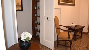 Una habitación con una silla de madera, una mesa pequeña con un cuenco, una puerta blanca y un estante con adornos.