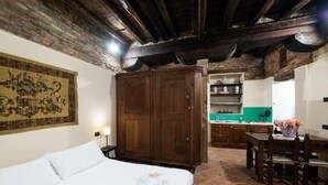 Un dormitorio con una cama, un armario de madera, una zona de cocina con encimera verde y una mesa de comedor con sillas.