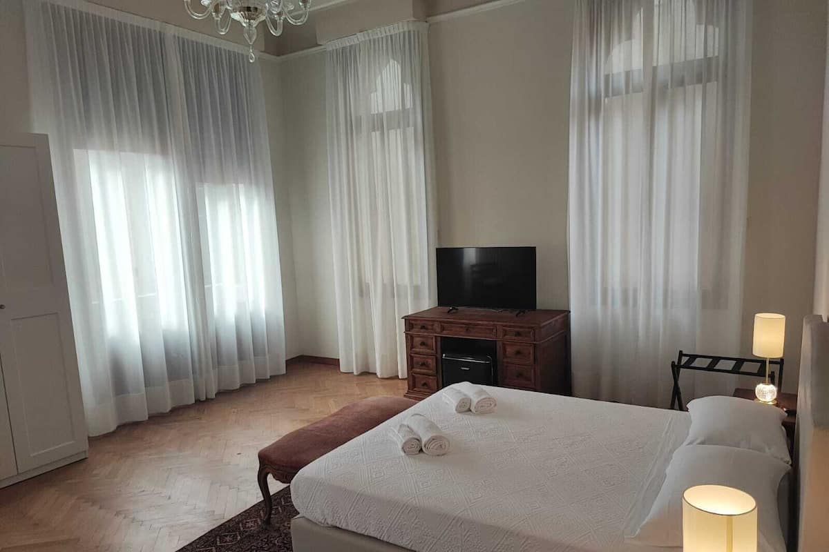 A hotel room with a large bed, a TV, a wooden dresser, and a nightstand with a lamp.