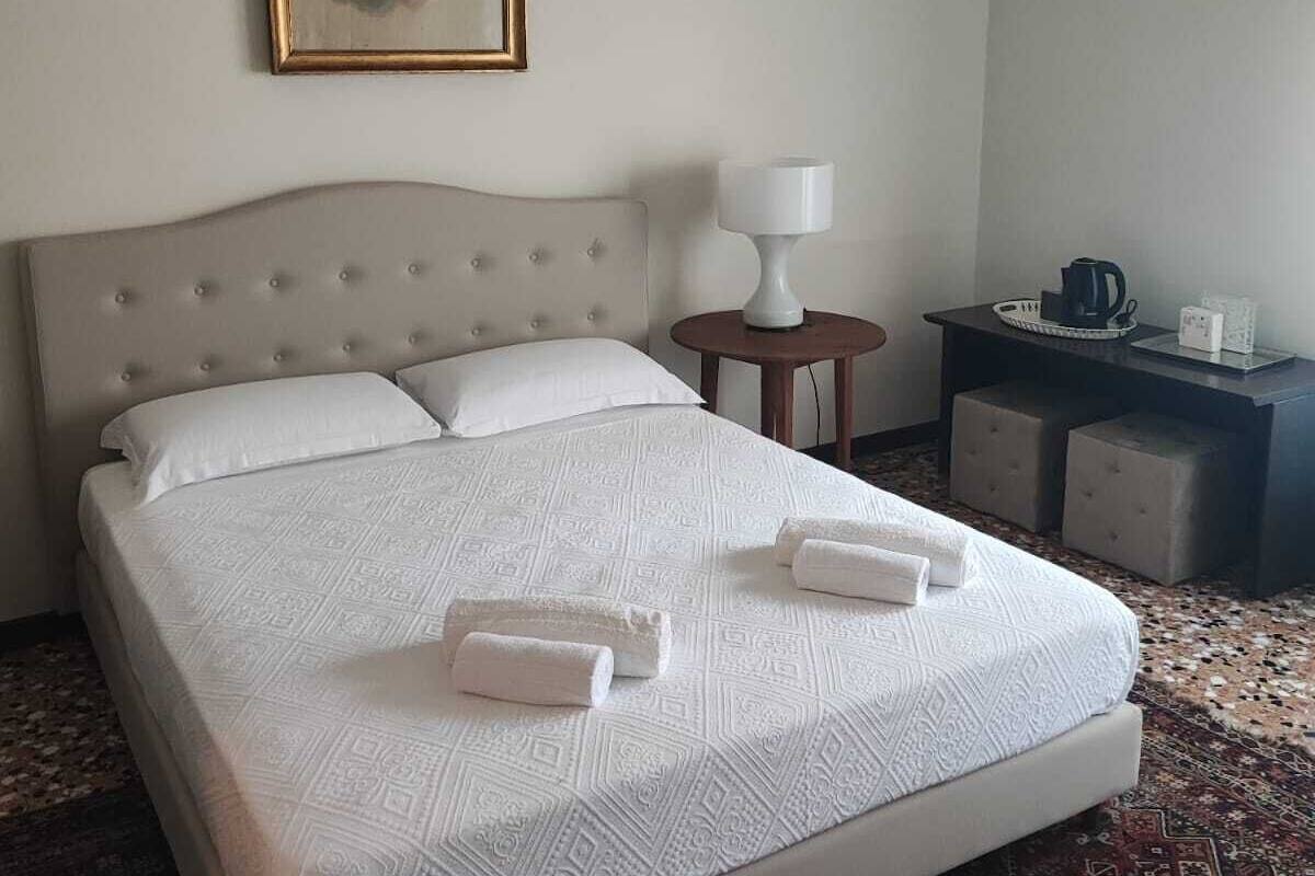 A hotel room with a large bed, a nightstand, a lamp, and a painting on the wall.
