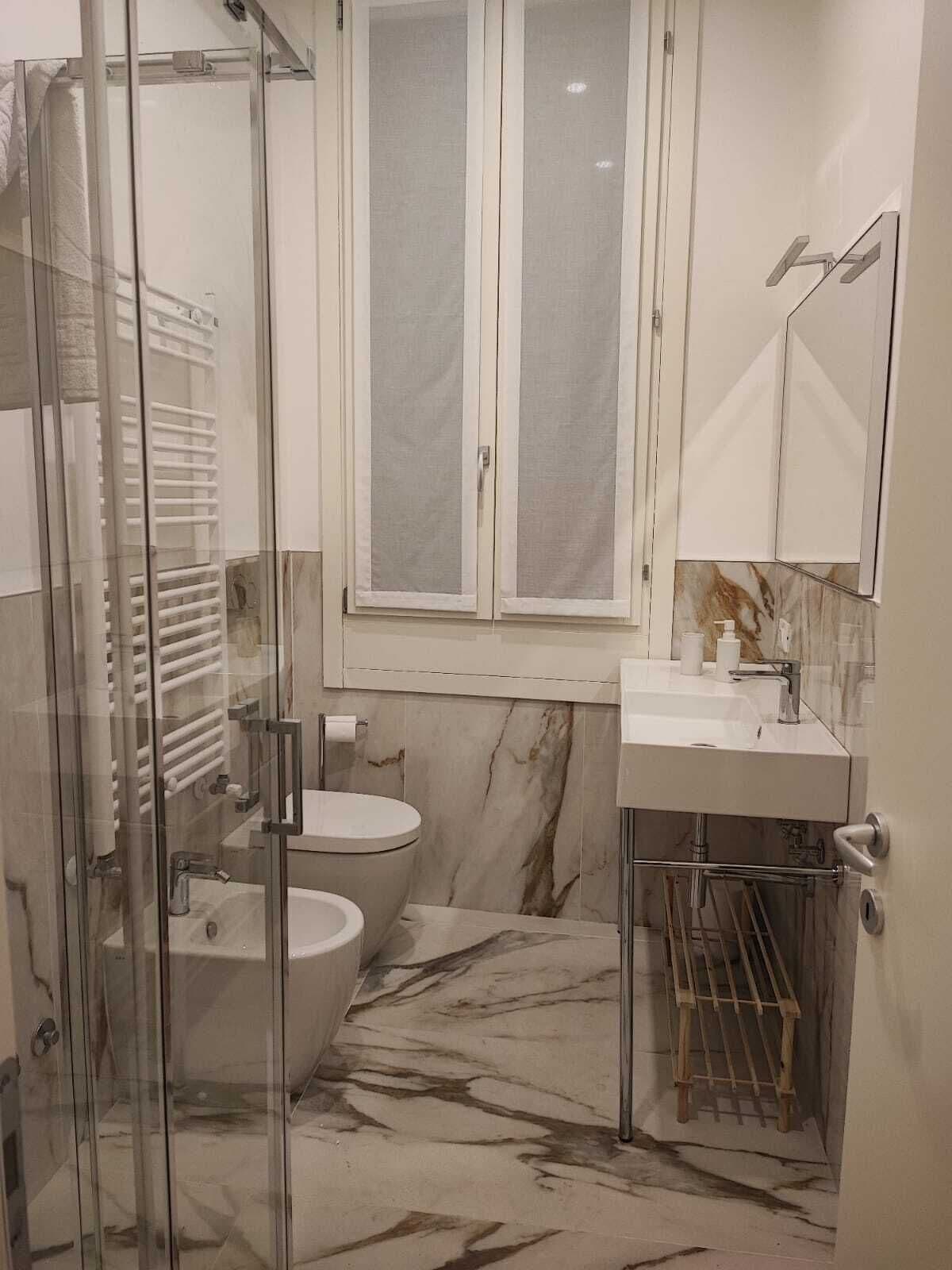 Moderni kylpyhuone, jossa on lasiseinäinen suihkukaappi, wc ja peilillä varustettu pesuallas.