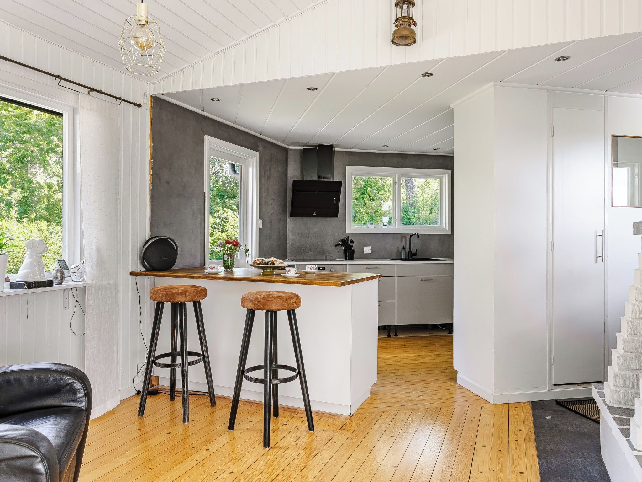 A modern kitchen with a central island, bar stools, and a view of greenery outside.