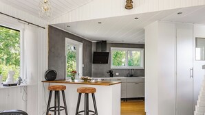 A modern kitchen with a central island, bar stools, and a view of greenery outside.
