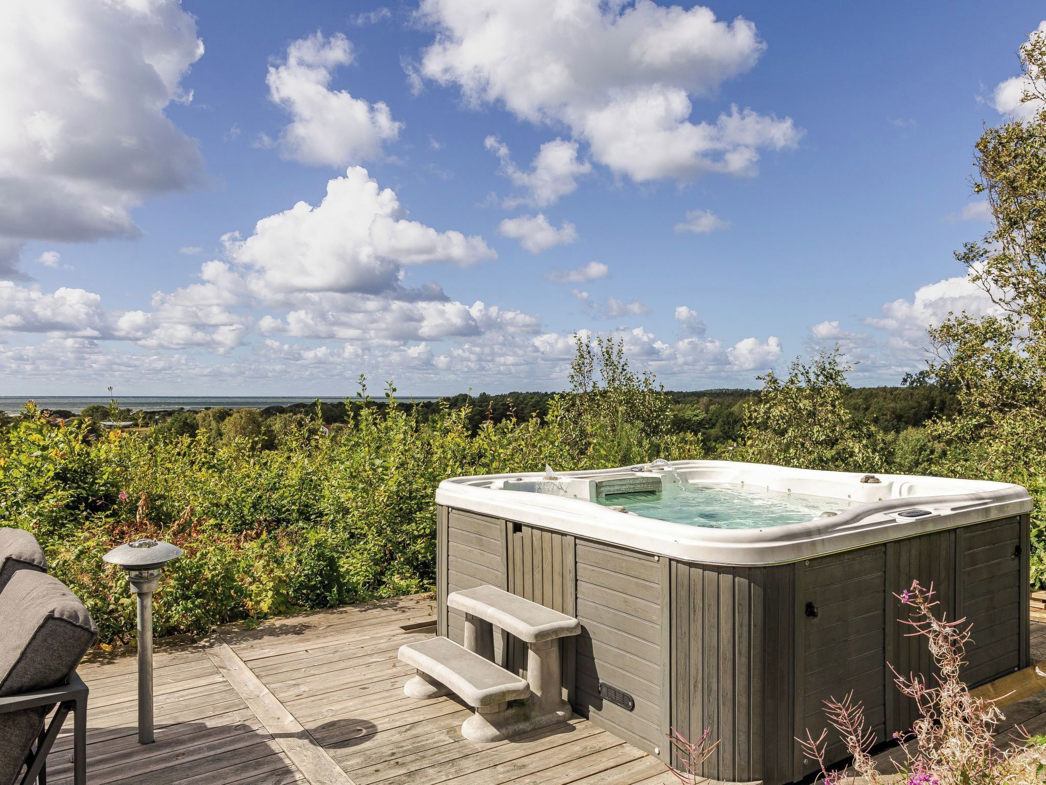 Un jacuzzi en una terraza de madera con vista al mar y nubes.