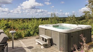 A hot tub on a wooden deck with a view of the sea and clouds.