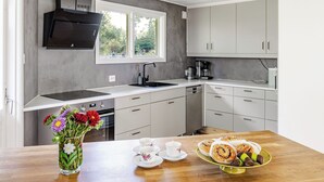 A modern kitchen with grey cabinets, a black range hood, a window, and a wooden table with pastries and a vase of flowers.
