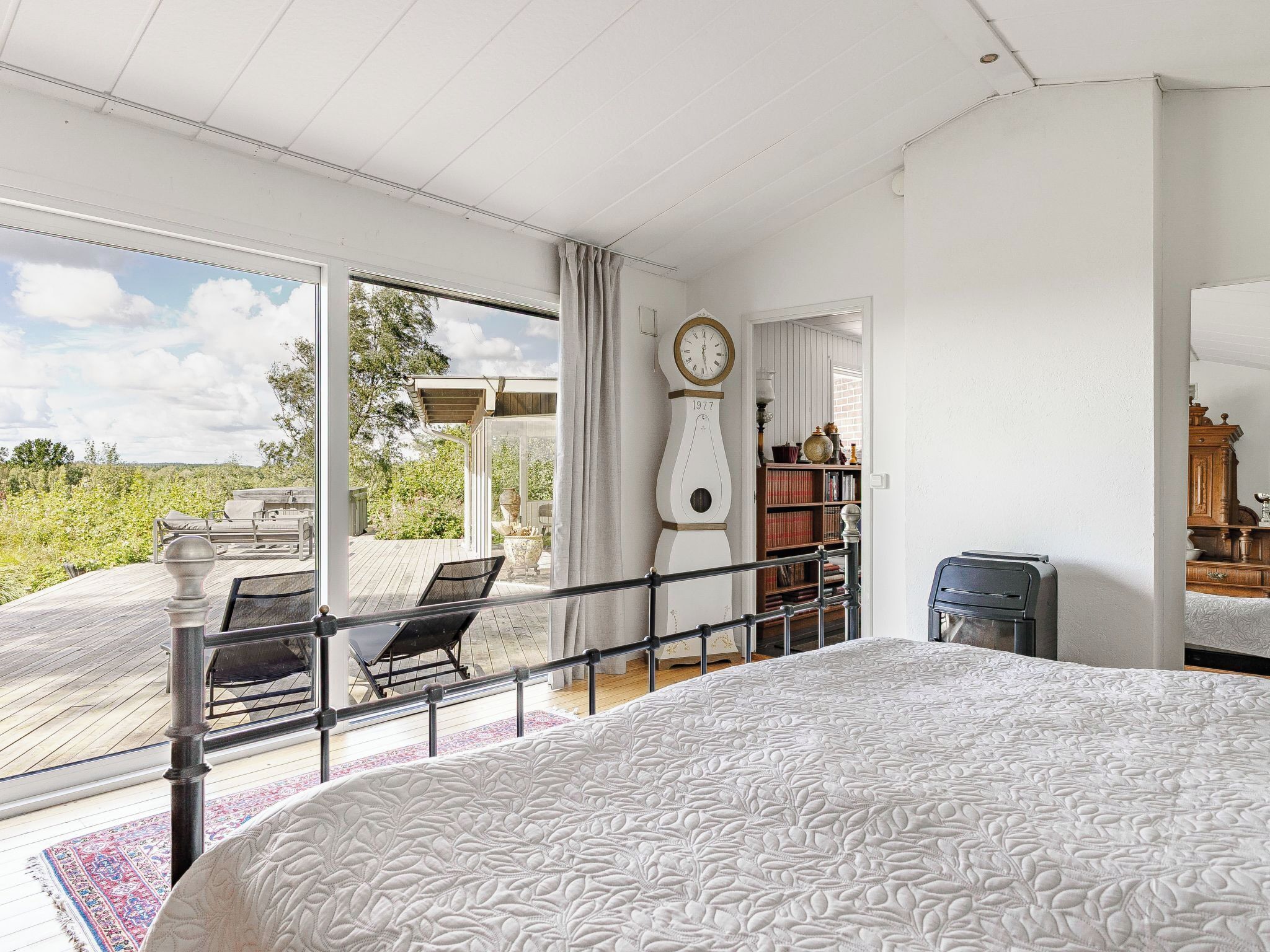 Une chambre spacieuse avec un grand lit, une vue sur l’extérieur, une terrasse en bois et une horloge au mur.
