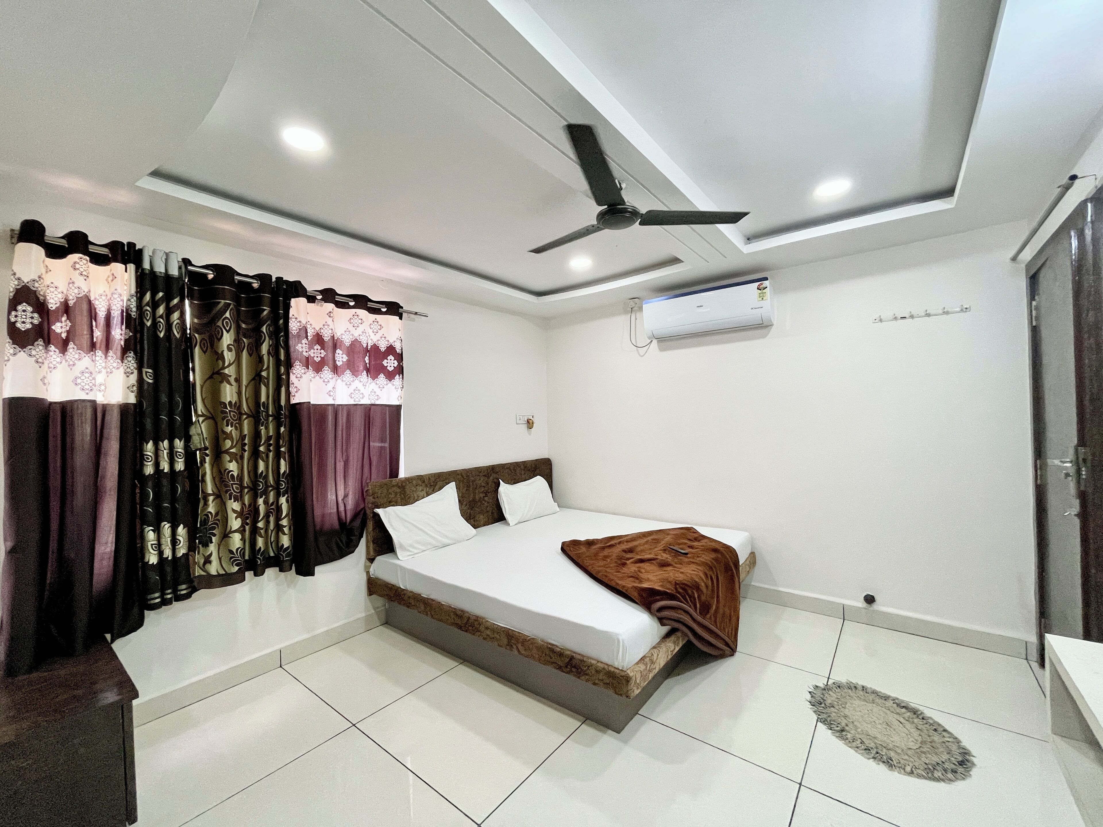 Un dormitorio con cama, cortinas, un equipo de aire acondicionado y un ventilador de techo.