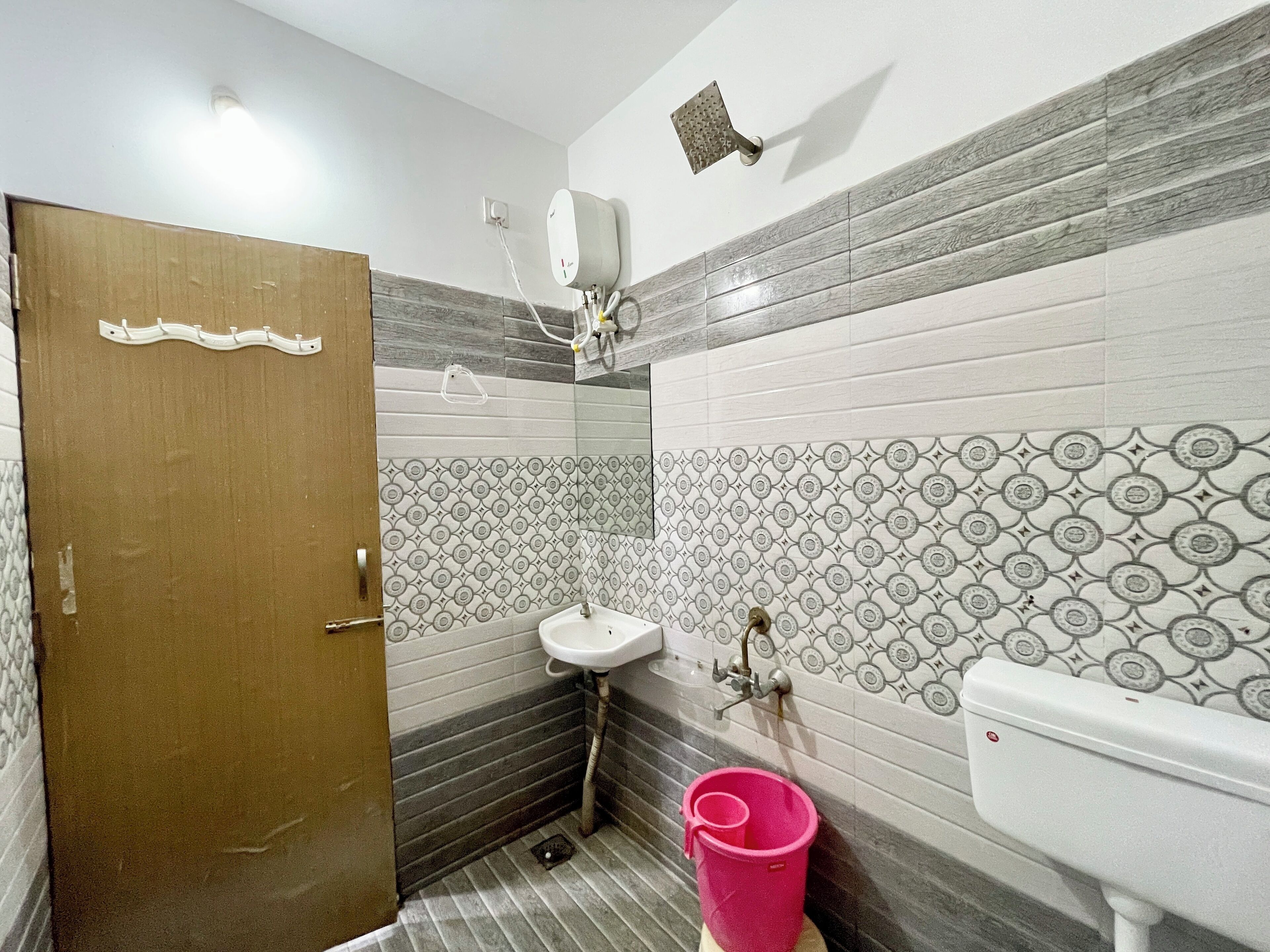 A bathroom with a wooden door, a sink, a toilet, and a pink bucket.