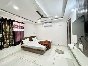 Un dormitorio moderno con cama, ventilador de techo, aire acondicionado, televisión y piso de baldosas.