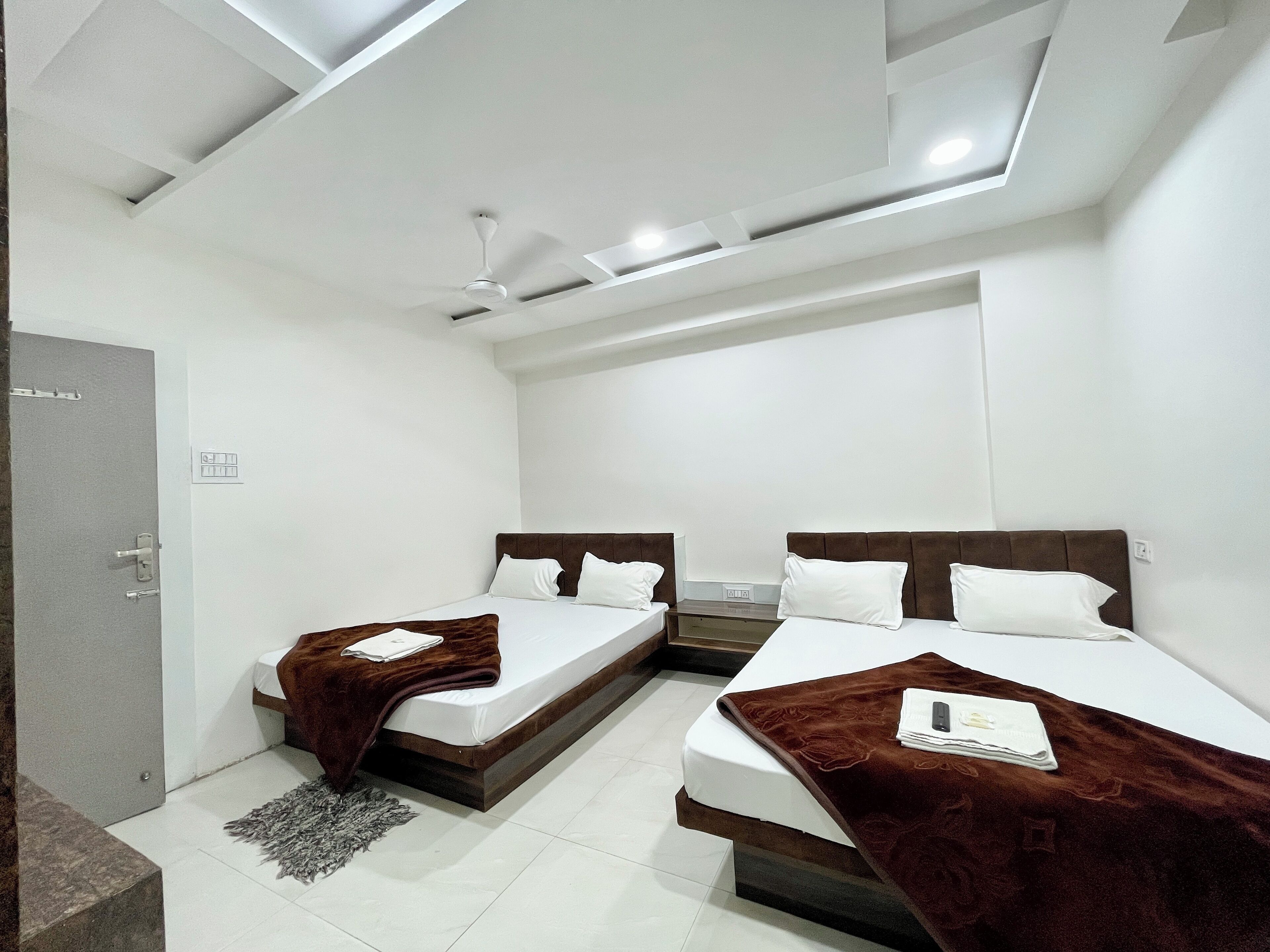 Una habitación de hotel moderna con dos camas, una puerta gris y un ventilador de techo.