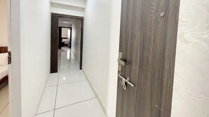 Un pasillo con puerta de madera, paredes blancas y suelo de baldosas.