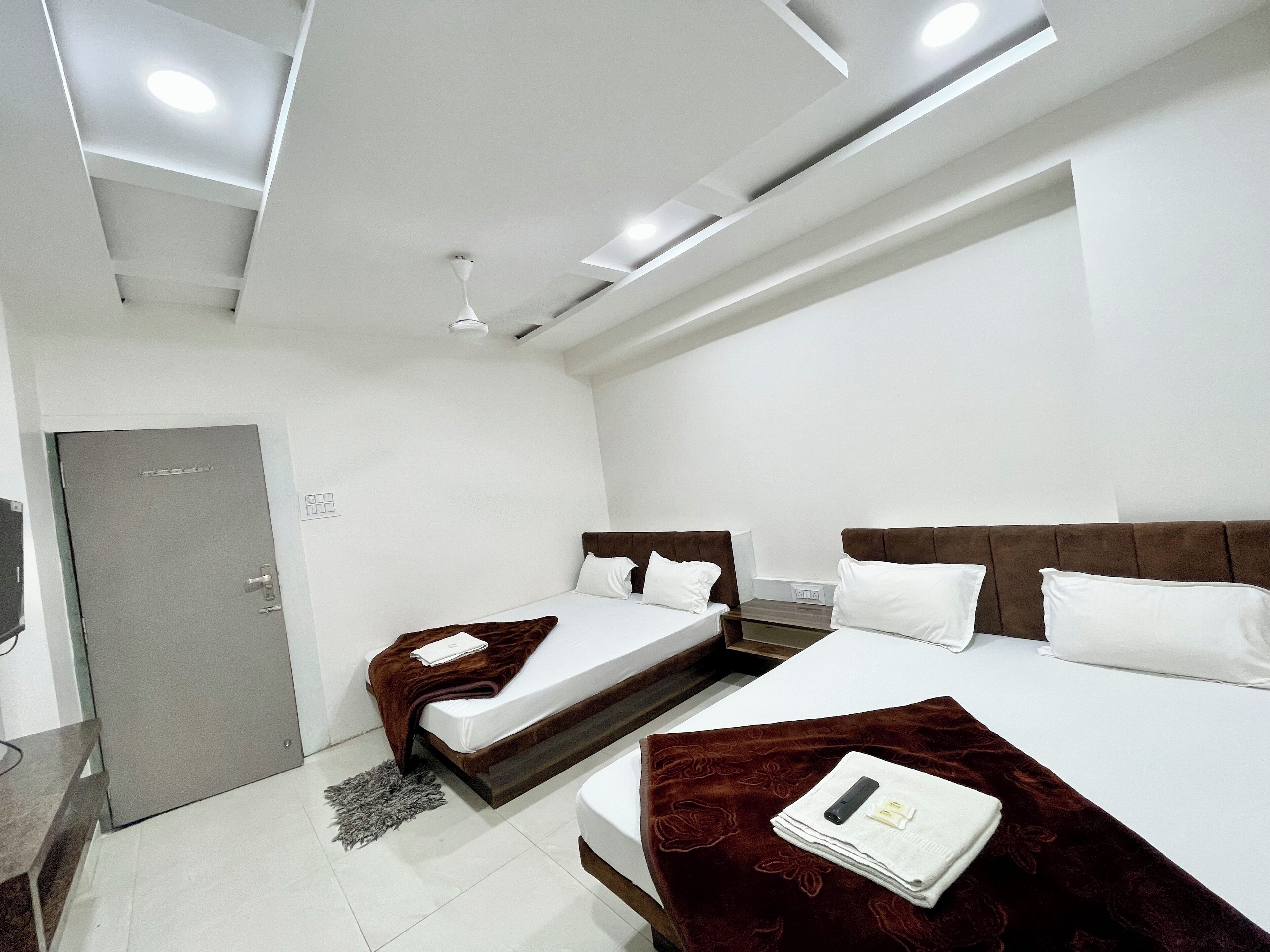 A modern hotel room with two beds, a grey door, and a ceiling with recessed lighting.