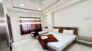 Una habitación de hotel con una cama grande, dos camas más pequeñas, un ventilador de techo y una ventana con cortinas.