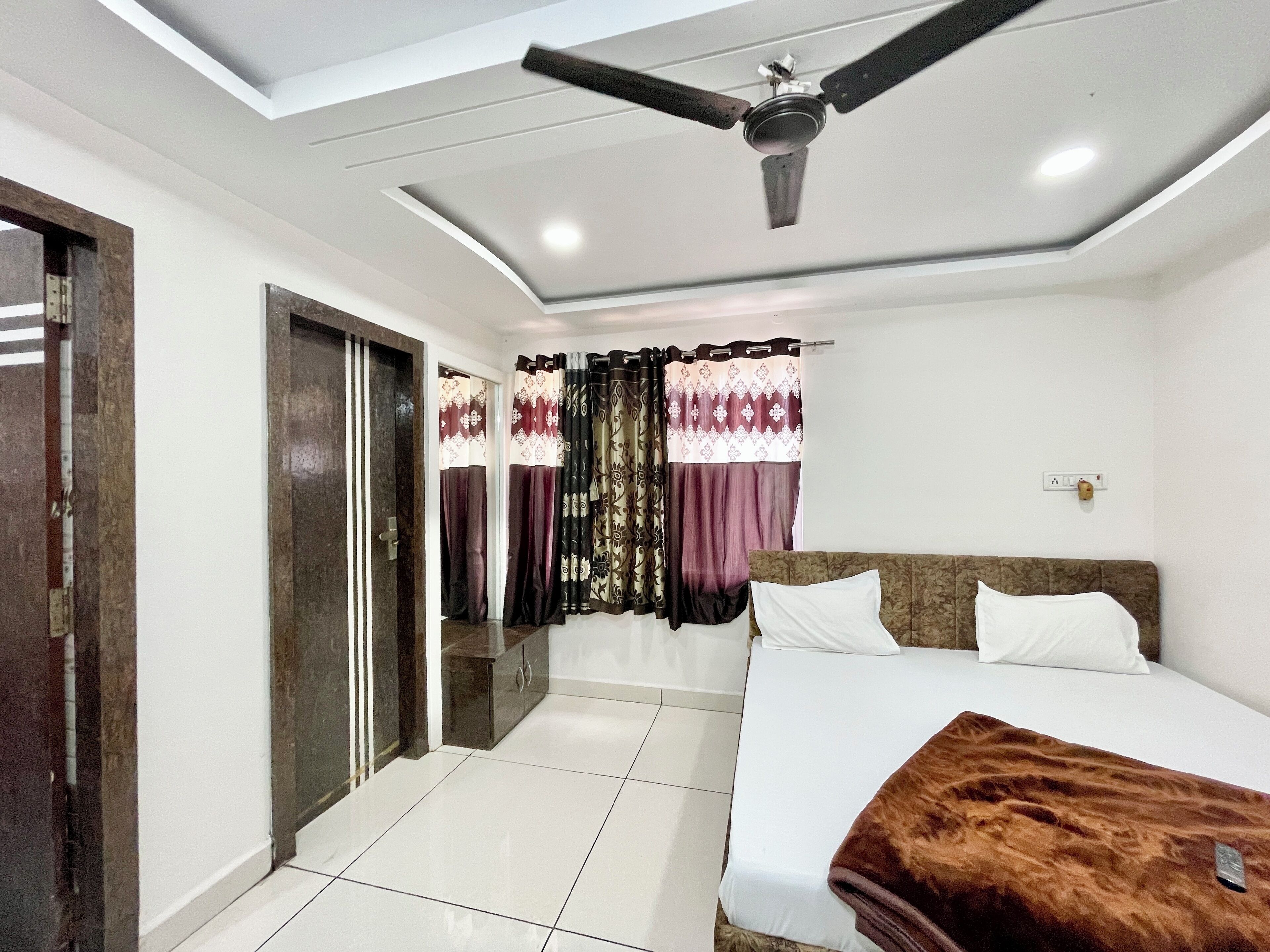 A bedroom with a bed, a ceiling fan, a window with curtains, and a door.