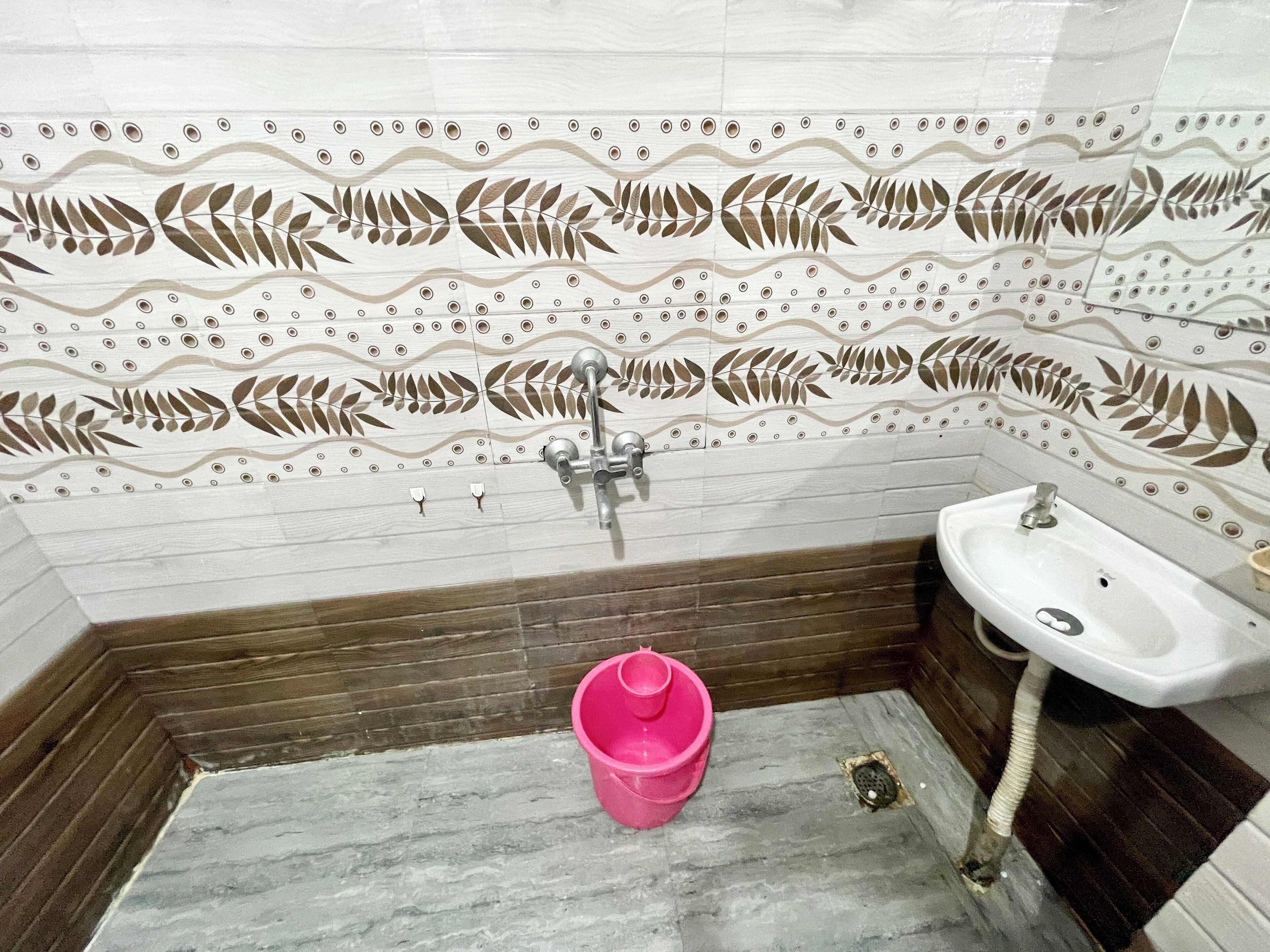 A bathroom with a patterned tile backsplash, a sink, and a pink bucket.