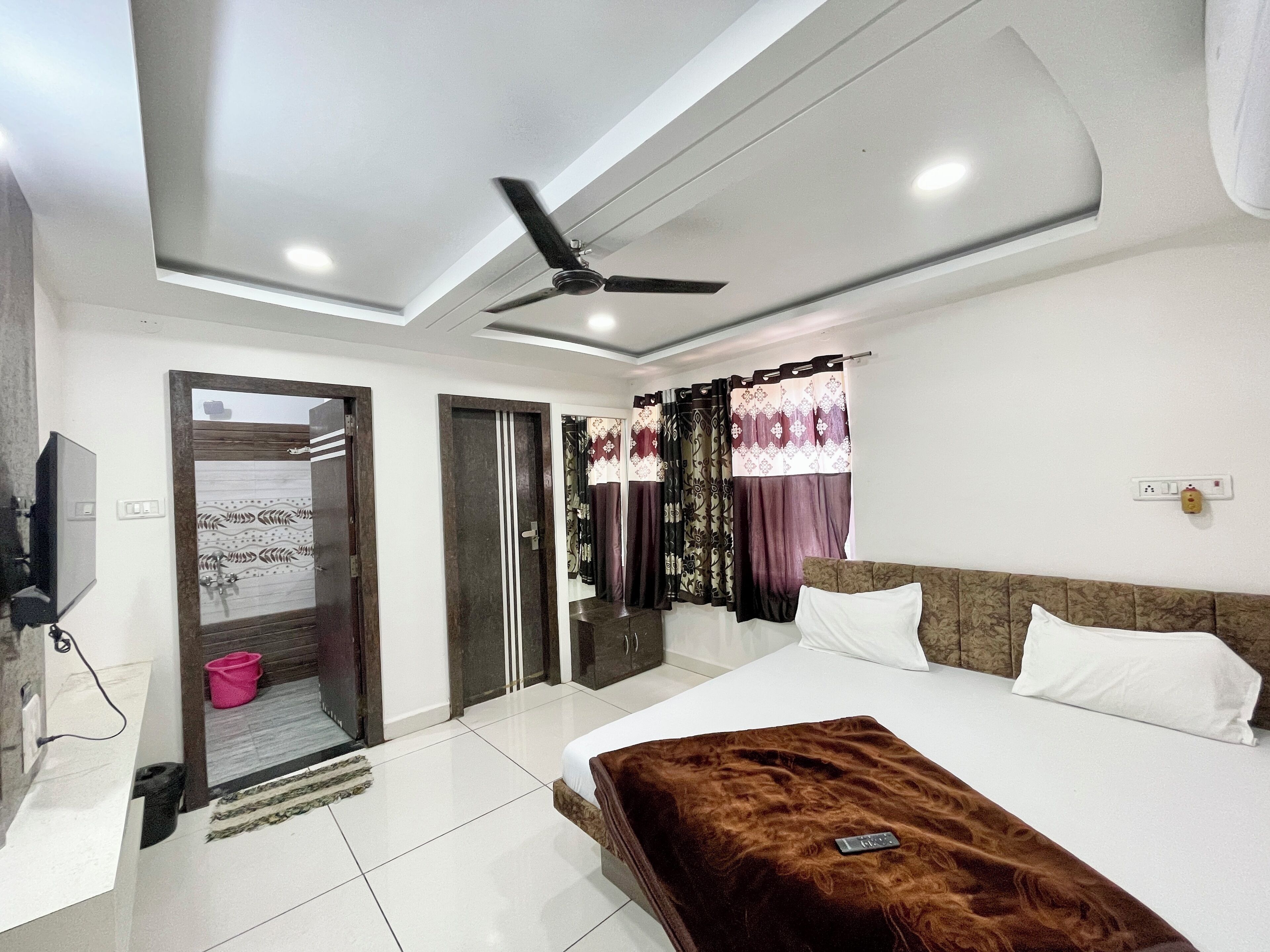 Een moderne slaapkamer met een groot bed, een plafondventilator en een aan de muur bevestigde televisie.