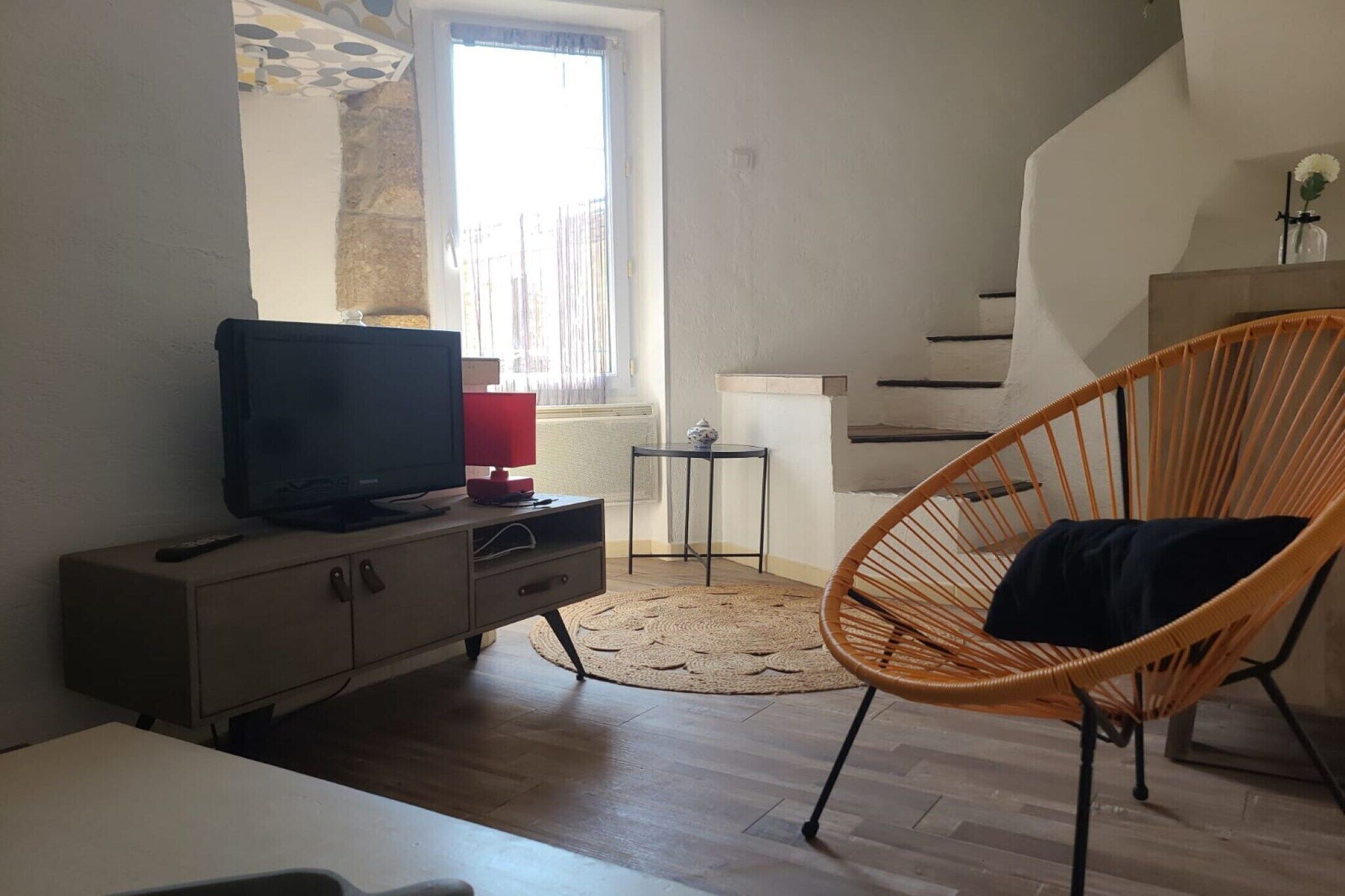 A living room with a television on a cabinet, a wicker chair, a small table, and a staircase.