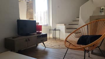 A living room with a television on a cabinet, a wicker chair, a small table, and a staircase.