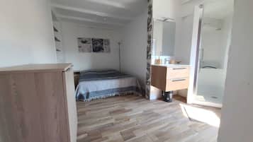 A bedroom with a bed, a wooden dresser, a mirror, and a door leading to a bathroom.