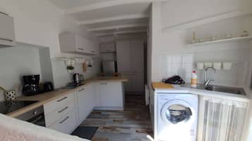 A compact kitchen with a washing machine, a coffee maker, and a small countertop.