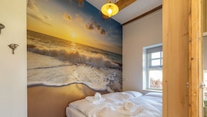 Ein Schlafzimmer mit einer Wandmalerei einer Strandansicht, einem Bett mit weißer Bettwäsche und einem Fenster mit Blick ins Freie.