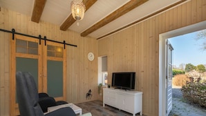 Ein Zimmer mit Holzwänden, einem großen Fenster, einem Fernseher und einer Schiebetür.