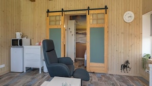 Ein gemütliches Zimmer mit Holzwänden, einem schwarzen Bürostuhl, einem kleinen Tisch mit Kerzen, einer Mikrowelle und einer Wanduhr.