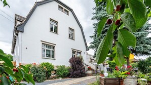 Een wit huis met een schuin dak, een grindpad en diverse planten en bloemen in de tuin.