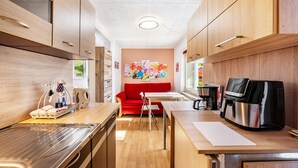 Een compacte keuken met houten kastjes, een rode bank, een koffieapparaat en een tafel.