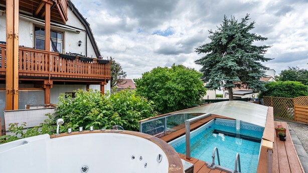Een woonhuis met een houten terras, een jacuzzi en een zwembad.