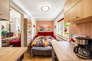Una habitación compacta con cama, una mesita, cafetera y ventana con una obra de arte.