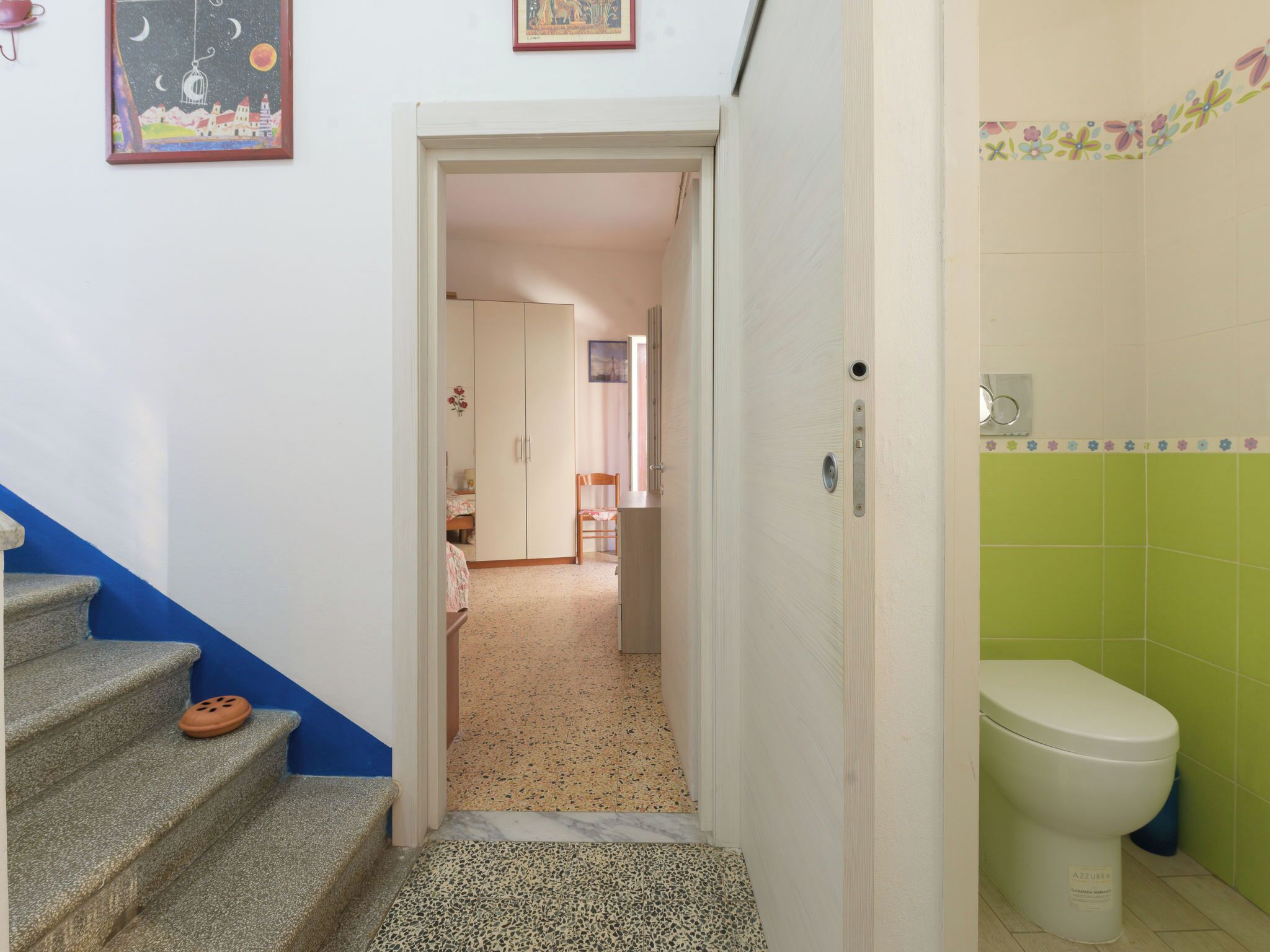 A hallway leading to a bedroom with a bed, a wardrobe, and a bathroom with a toilet.