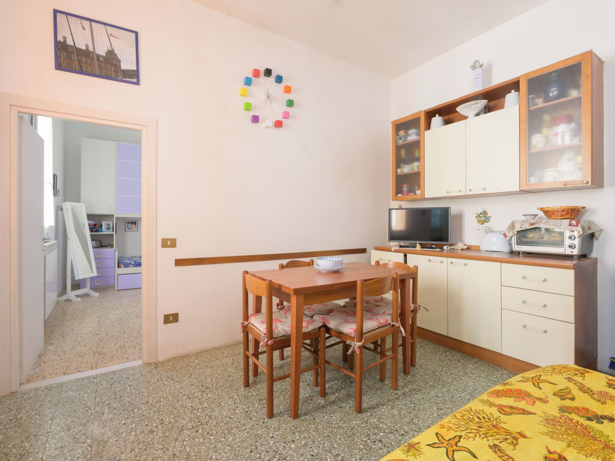 A compact room with a wooden dining table, chairs, a small kitchen area with a microwave, and a television.