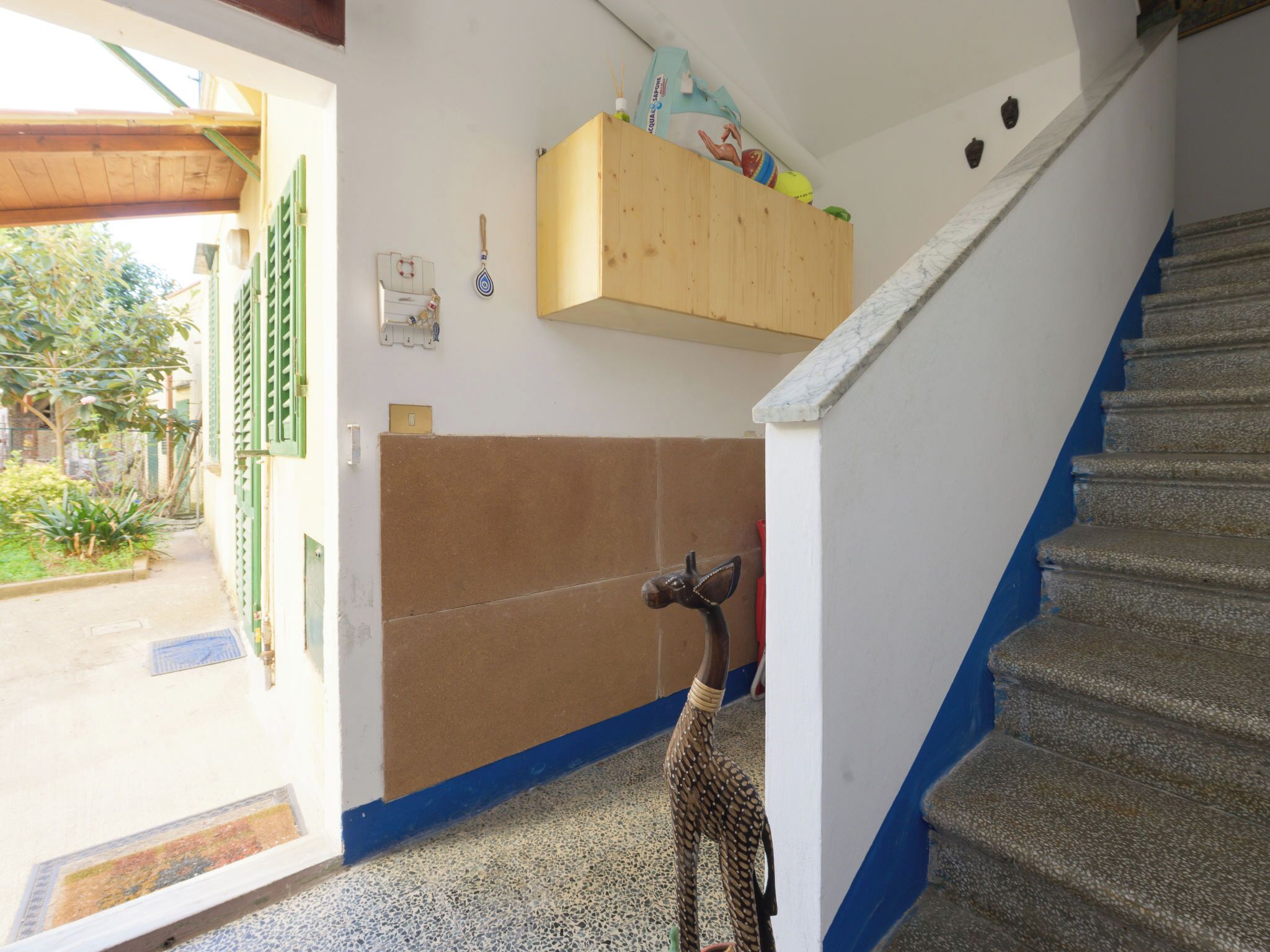 Un escalier menant à un deuxième étage, une armoire en bois sur laquelle sont posés divers objets, et une figurine d’animal décorative sur le sol.