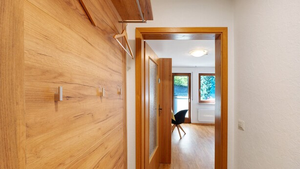 Un couloir aux murs en bois, une porte donnant sur une pièce et une chaise au loin.