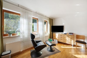 Un salon moderne avec un fauteuil noir, un banc en bois, un téléviseur, un meuble et une fenêtre avec des rideaux.