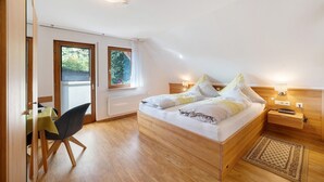 Une chambre avec un lit en bois, un bureau et une chaise, une fenêtre donnant sur un paysage verdoyant et un luminaire au plafond.