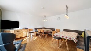 Un salon moderne doté d’un téléviseur à écran plat, de meubles en bois, d’une table à manger avec des chaises et de luminaires suspendus.