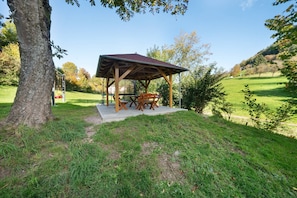 Un pavillon en bois, doté d’un toit, entouré d’herbe et d’arbres.