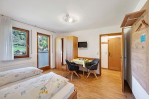 Une chambre avec deux lits, une armoire en bois, un bureau avec des chaises, une télévision et une vue sur un jardin.